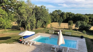 Ein rechteckiger Swimmingpool mit gefliestem Sonnendeck, umgeben von weißen Liegestühlen und einem Sonnenschirm.