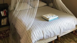 Ein Bett mit Moskitonetz, gestreifter Bettwäsche und einem Buch darauf.