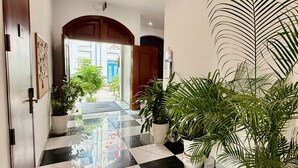 Un corridoio d'hotel con pavimento a scacchi, piante in vaso e vista sull'esterno.