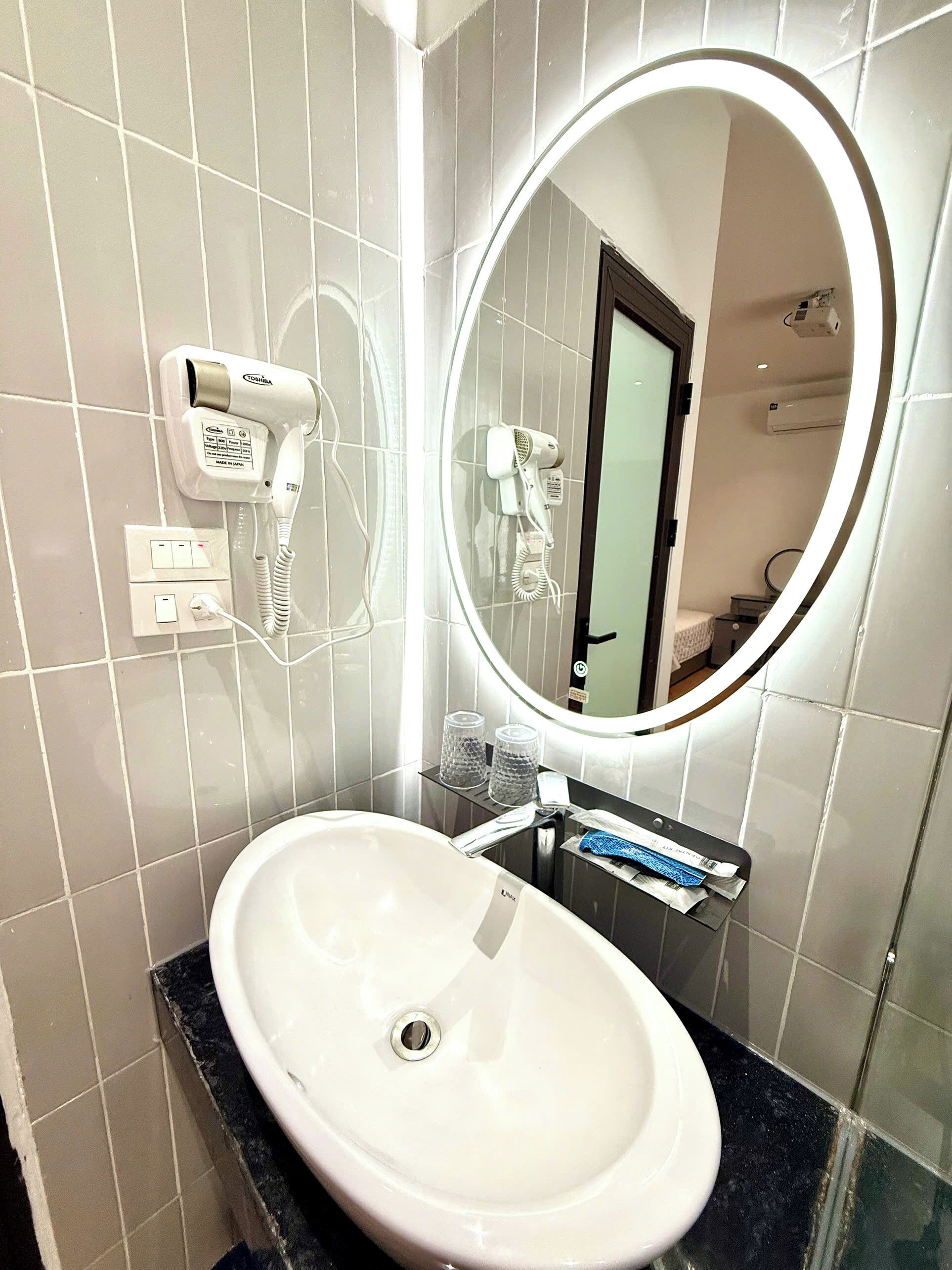 A bathroom with a white sink, a mirror with a light, and two hair dryers mounted on the wall.