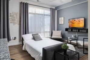 A modern hotel room with a bed, a TV, a desk, and a chair.