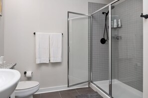 A modern bathroom with a glass-enclosed shower, a toilet, and a sink.