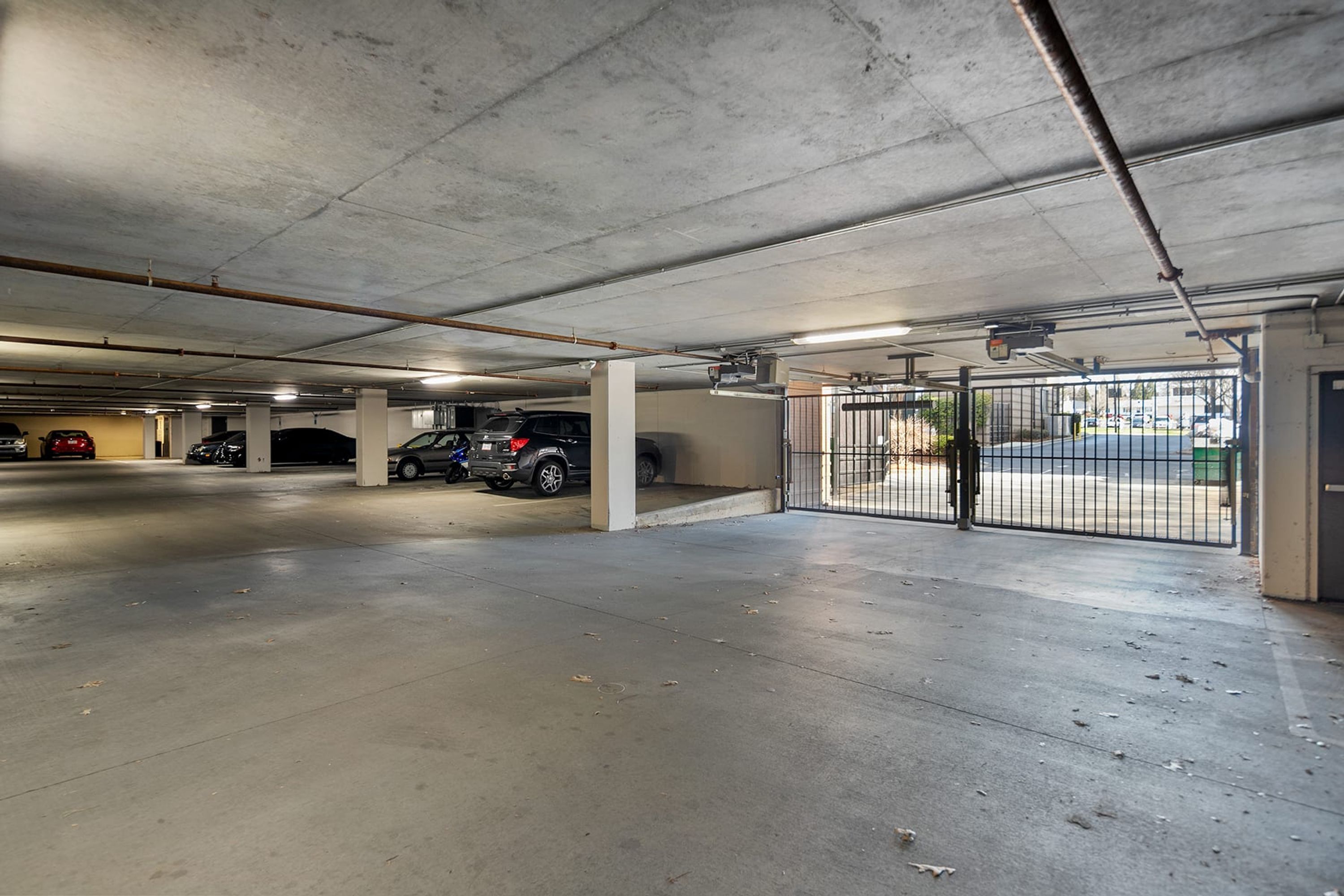 A multi-level parking garage with concrete floors and columns, a gated entrance, and several parked vehicles.