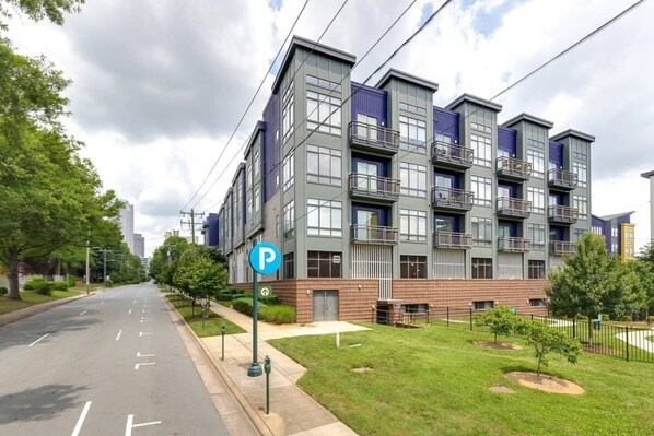 A multi-story residential building with a parking sign, a grassy area, and a sidewalk.