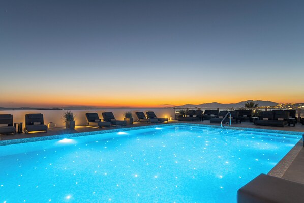 An infinity pool with lounge chairs and a view of the sunset over the water. - Rochari  (Mykonos)