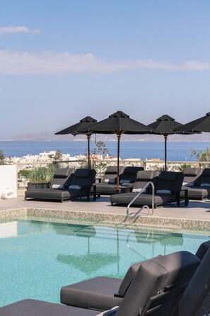 A poolside area with lounge chairs and umbrellas, overlooking a body of water and distant land. - Rochari  (Mykonos)