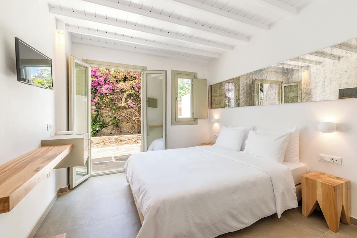 A modern bedroom with a large bed, a wooden bedside table, a nightstand, and a TV mounted on the wall.