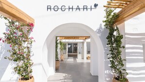 Una entrada con una pérgola de madera y plantas en macetas que conduce a un edificio con el nombre "ROCHARI" en la parte superior.