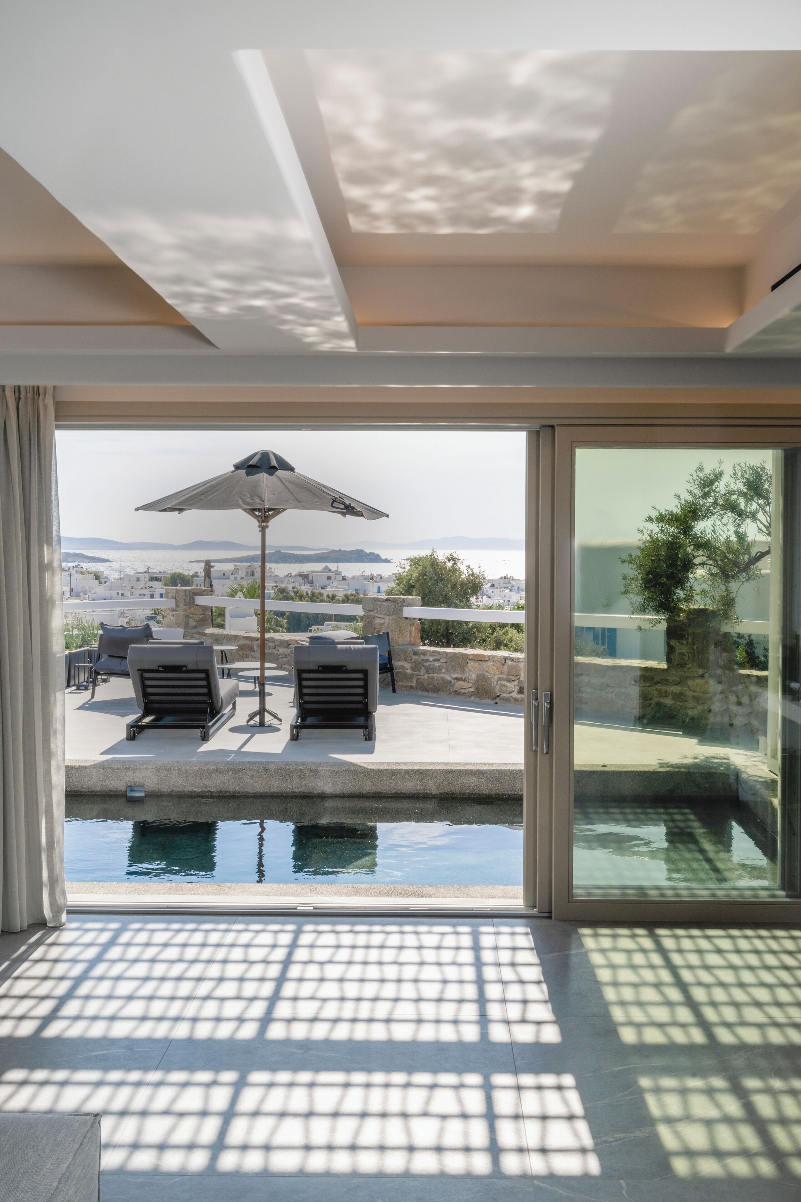 Una habitación moderna con puerta de vidrio que da a una zona de piscina, con tumbonas y una sombrilla.