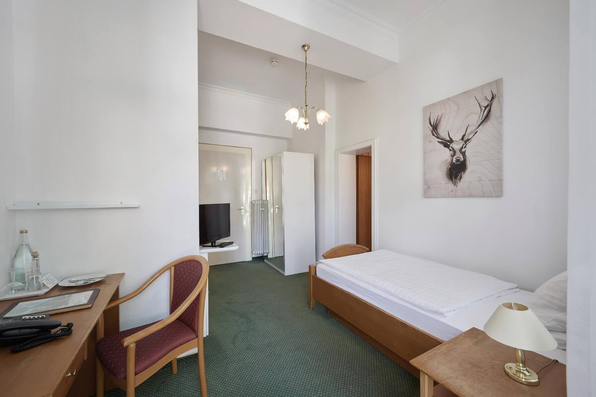 Une chambre d’hôtel avec un lit, un bureau et une chaise, une télévision, une lampe et un tableau au mur.