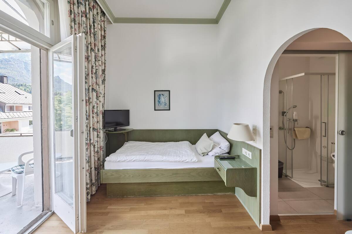 Une chambre à coucher comprenant un lit, une télévision, une table de chevet, une fenêtre avec des rideaux et une vue sur l’extérieur.