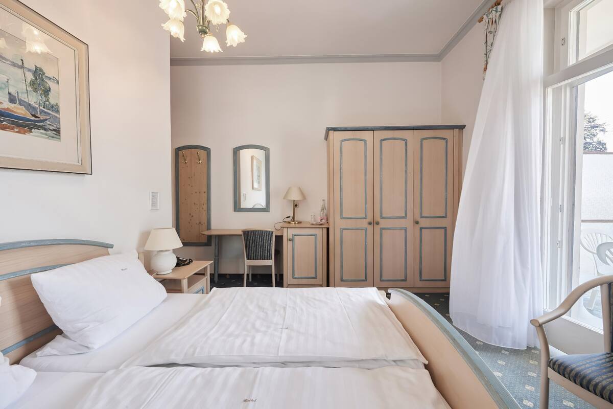 Une chambre à coucher bien rangée, avec un lit, une table de chevet, une lampe, une chaise, une armoire et un tableau encadré accroché au mur.