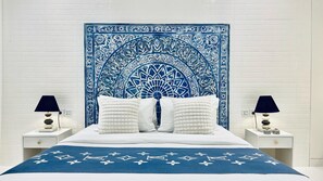 Un lit avec une tête de lit à motifs bleus et blancs, des oreillers blancs et une couvre-lit bleue à motifs blancs. Il y a deux tables de chevet avec des lampes et des objets décoratifs.