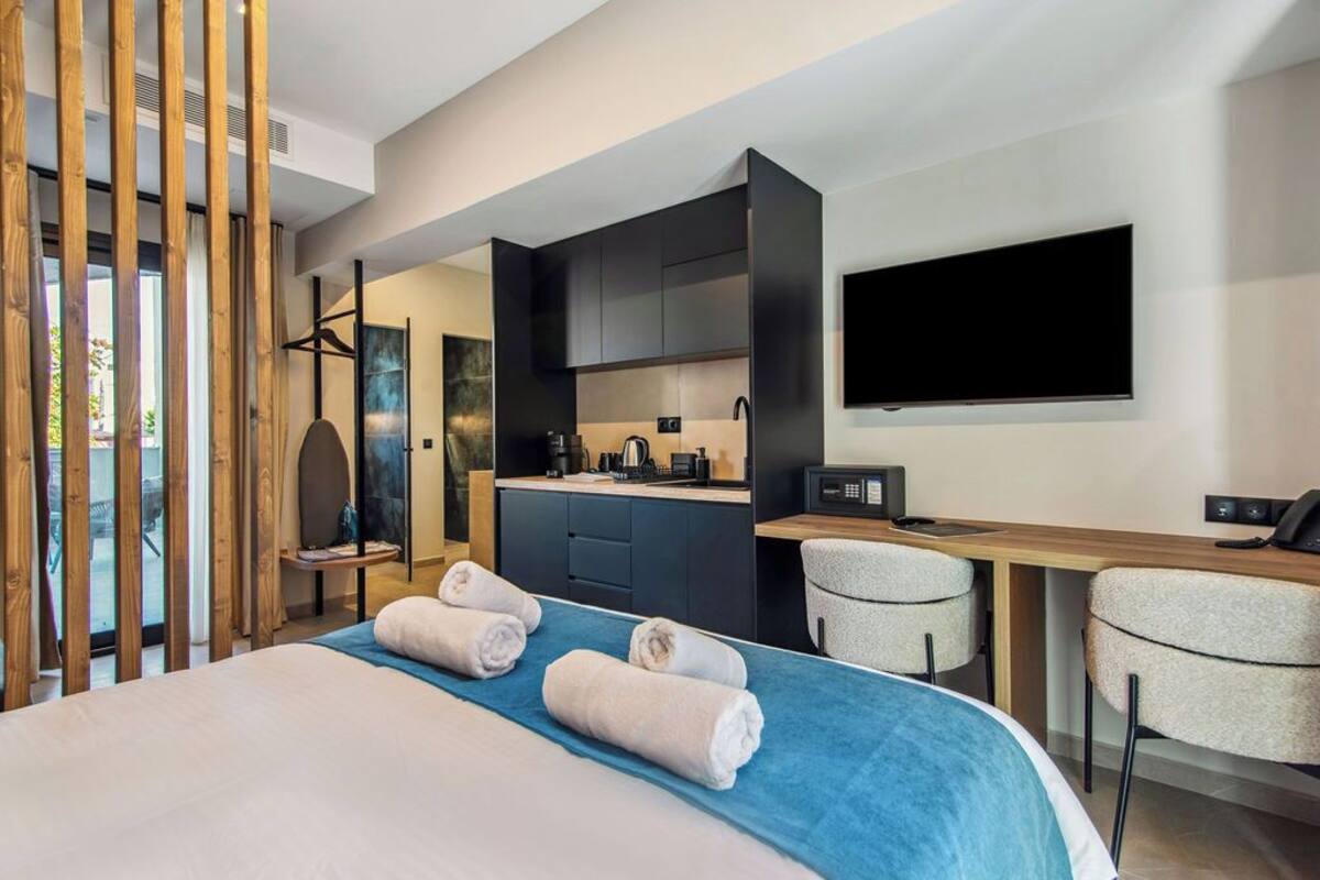 Een moderne hotelkamer met een bed, een bureau, een stoel, een televisie en een kitchenette.
