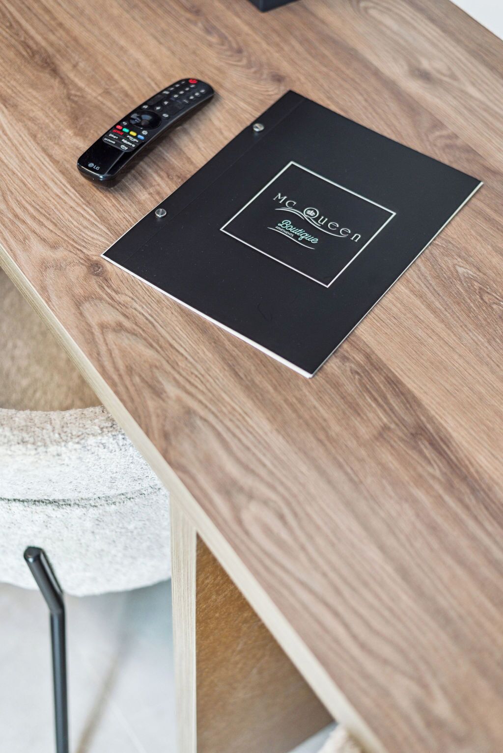 Une table en bois, avec une télécommande et un dossier noir portant l’inscription « Ma Queen Boutique ».