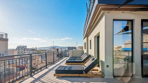A rooftop terrace with sun loungers, a glass door, and a view of the cityscape. - Mc Queen Apartments (Athens)