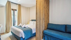 A modern hotel room with a bed, a blue sofa, and a wooden partition. - Mc Queen Apartments (Athens)