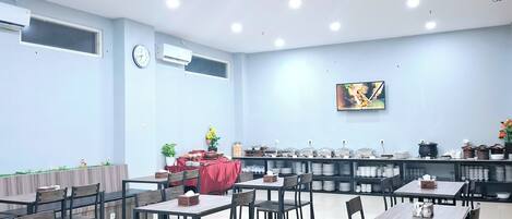A spacious dining area with multiple tables and chairs, a clock, and a television on the wall.