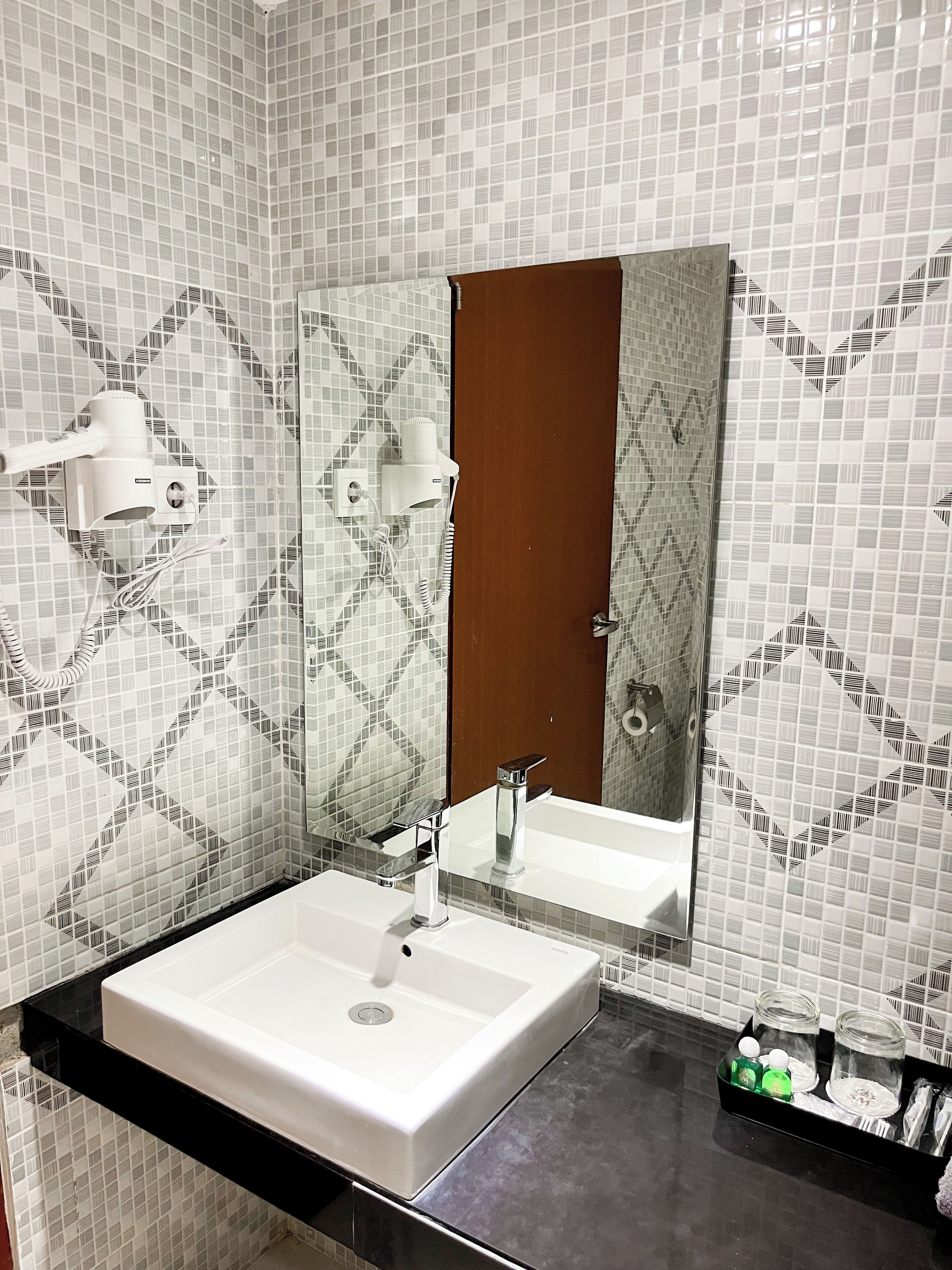 Un bagno con un lavandino bianco, uno specchio e una parete rivestita di piastrelle decorate.