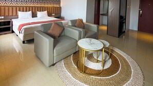 A modern hotel room with a large bed, a sofa, a small round table, and a patterned rug. - SM Tower Hotel & Convention Center Berau (Tanjung Redeb)
