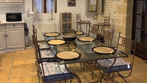 A dining area with a glass table surrounded by chairs, a kitchen area with cabinets, a microwave, and a stone wall. - DOMAINE AUX ETOILES (Salviac)