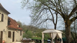 A rustic stone building with a tiled roof, a covered outdoor seating area, and a large tree in the background. - DOMAINE AUX ETOILES (Salviac)