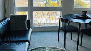Moderni huone, jossa on musta nahkasohva, pyöreä pöytä tuoleineen sekä suuret ikkunat, joista avautuu näkymä vuorille ja järvelle.