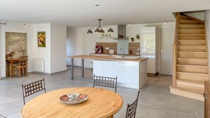A modern kitchen with a central island, white cabinetry, and a wooden staircase. - Chez mamie (Montdragon)