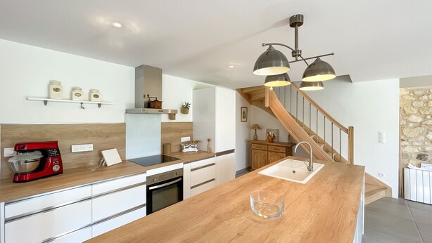 A modern kitchen with a central island, wooden cabinets, a red mixer, and a staircase leading to another level. - Chez mamie (Montdragon)