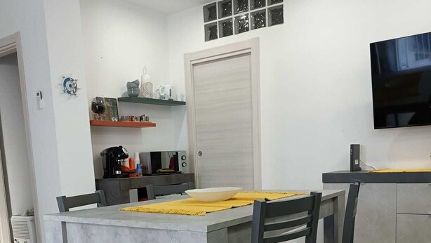 Une cuisine moderne avec un coin repas, comprenant une table grise, des chaises noires et un set de table jaune.