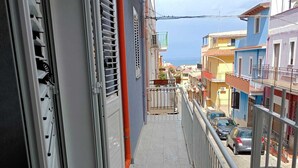Un balcon étroit doté d’une rambarde en métal, une porte avec une poignée et une vue sur des bâtiments aux couleurs vives et une étendue d’eau au loin.