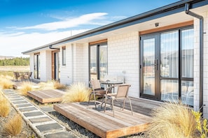 Ein modernes Haus mit einer Terrassenanlage, Möbeln für draußen und Blick auf die umliegende Landschaft.