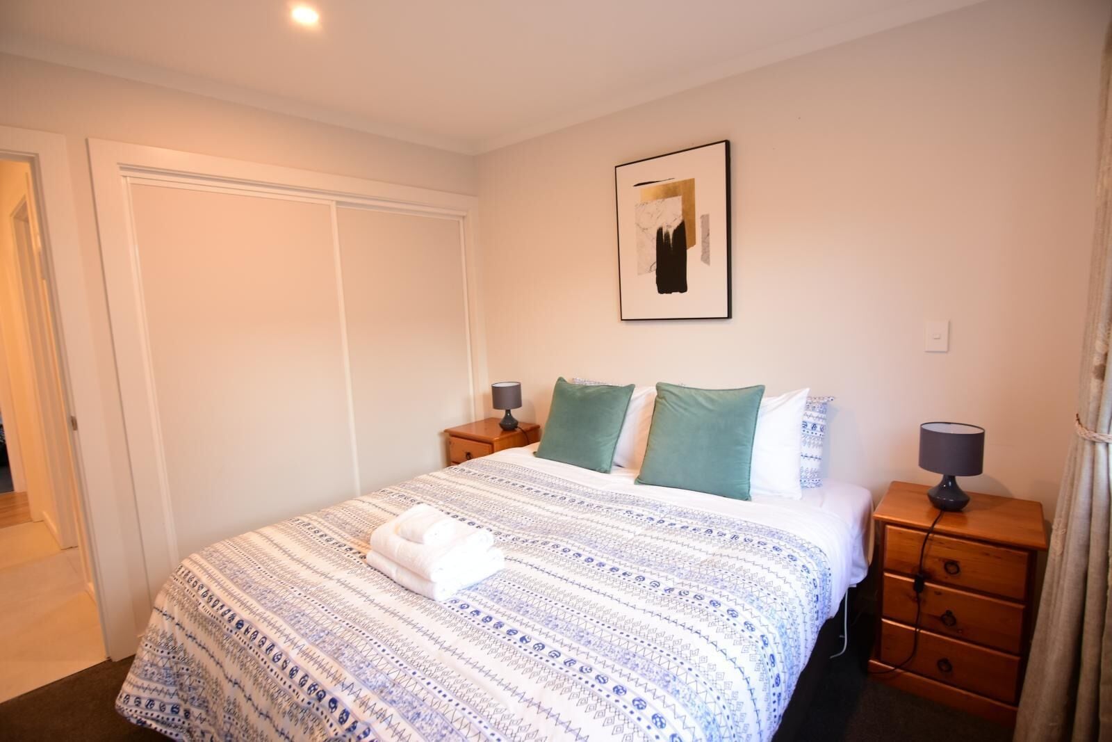 Habitación de hotel con una cama grande, dos mesitas de noche, un cuadro enmarcado en la pared y una puerta a la izquierda.