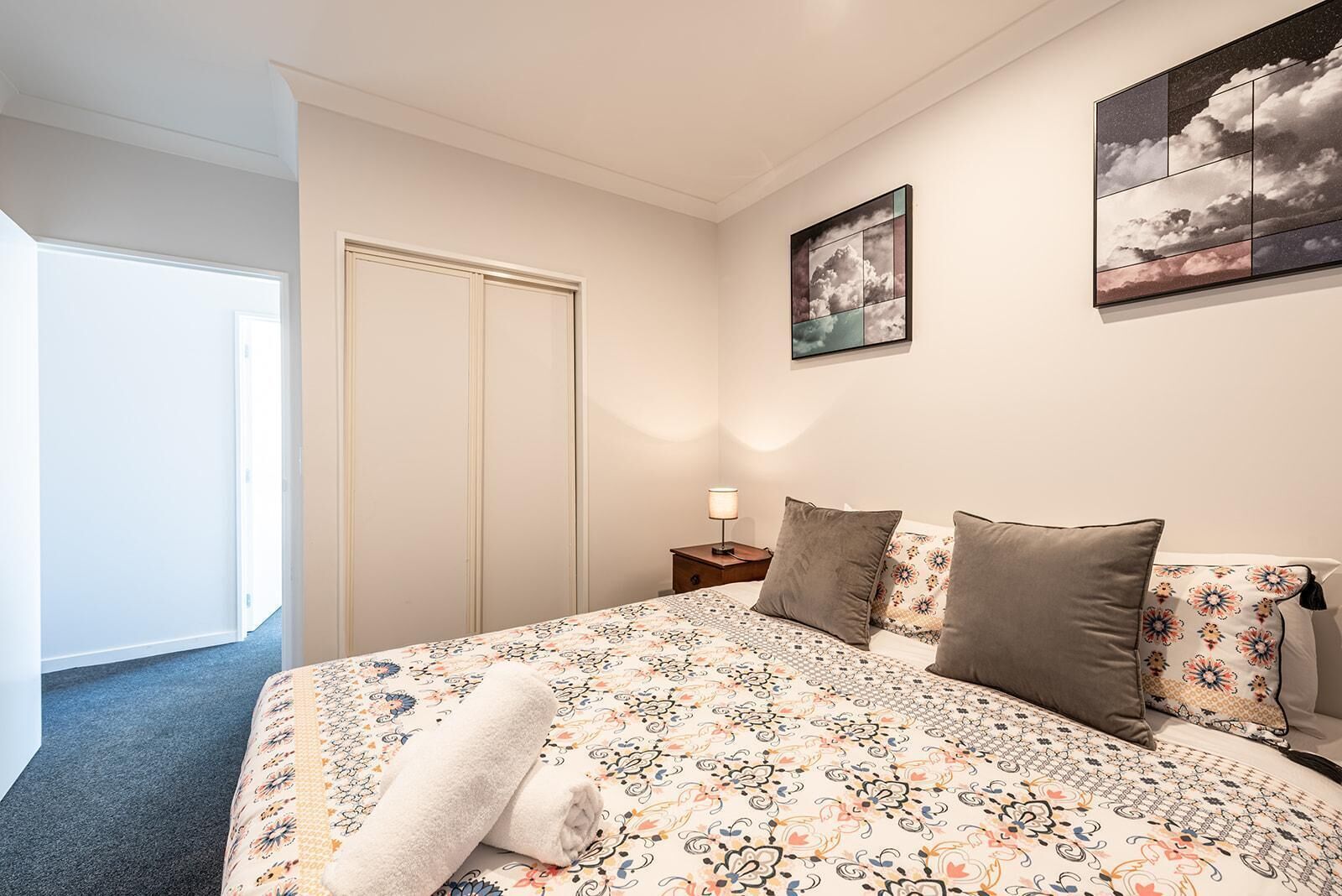 A bedroom with a bed, a nightstand, a lamp, a door, and a framed picture on the wall.