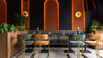 Ein modernes Restaurant mit einer langen Theke, grünen Sitzflächen mit Polstern und warmer Beleuchtung.