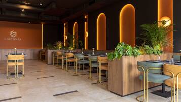 Un restaurante moderno con una barra larga, varias zonas de estar y una iluminación cálida.
