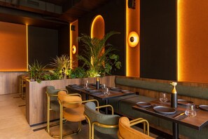 A restaurant interior with wooden tables, cushioned chairs, and warm lighting. -  Diagonal Hotel (Hjar Ennhal)