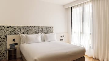 A neatly made bed with white linens, a headboard with a floral pattern, a bedside telephone, and a nightstand.