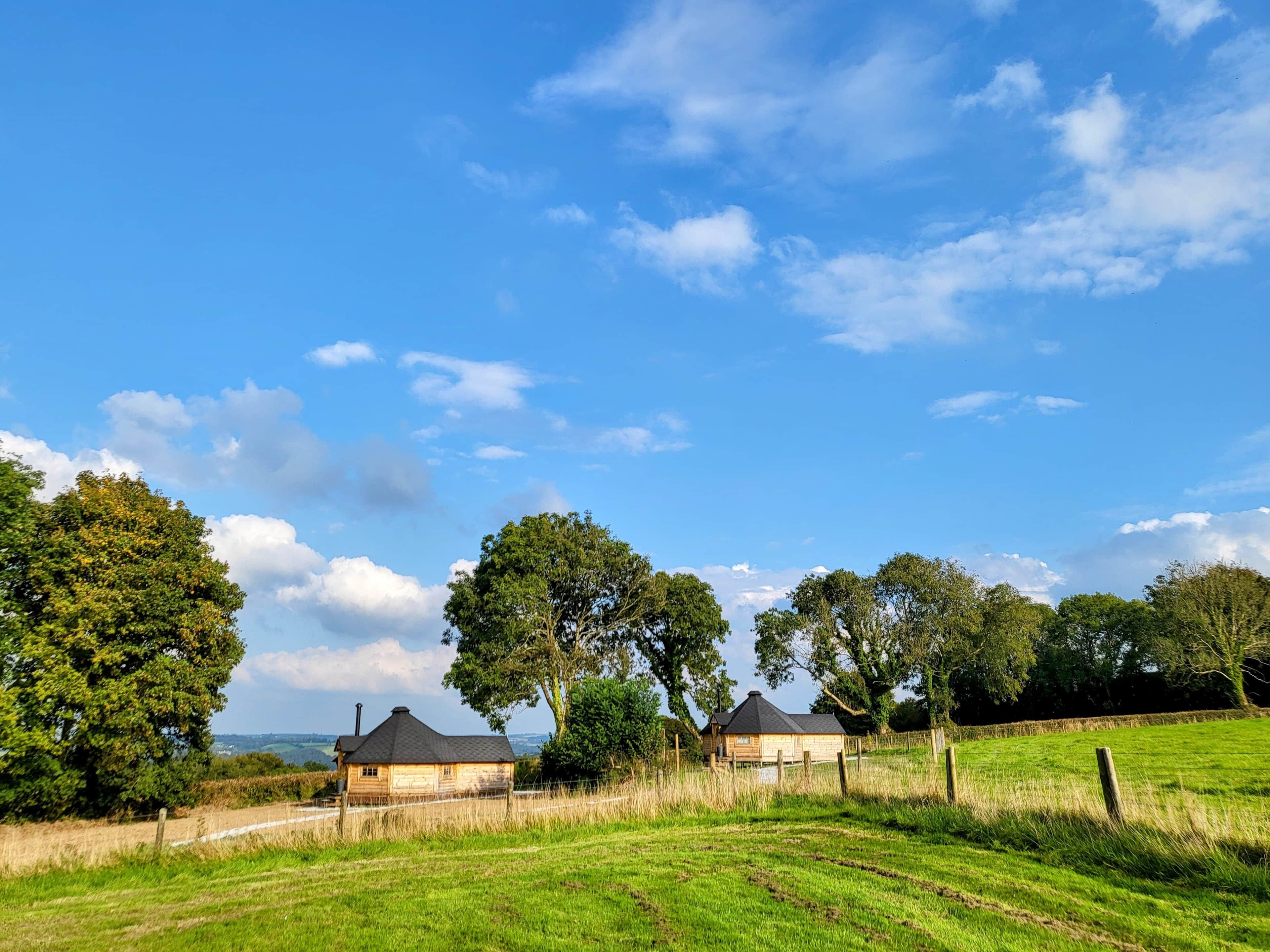 Paisaje rural con dos casas de madera, cielo despejado y un campo cubierto de hierba.
