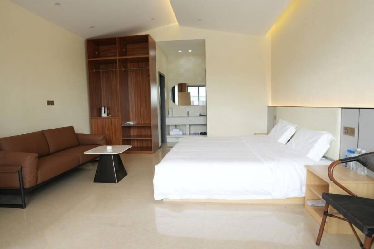 A modern hotel room with a large bed, a brown sofa, a small table, and a wooden wardrobe.