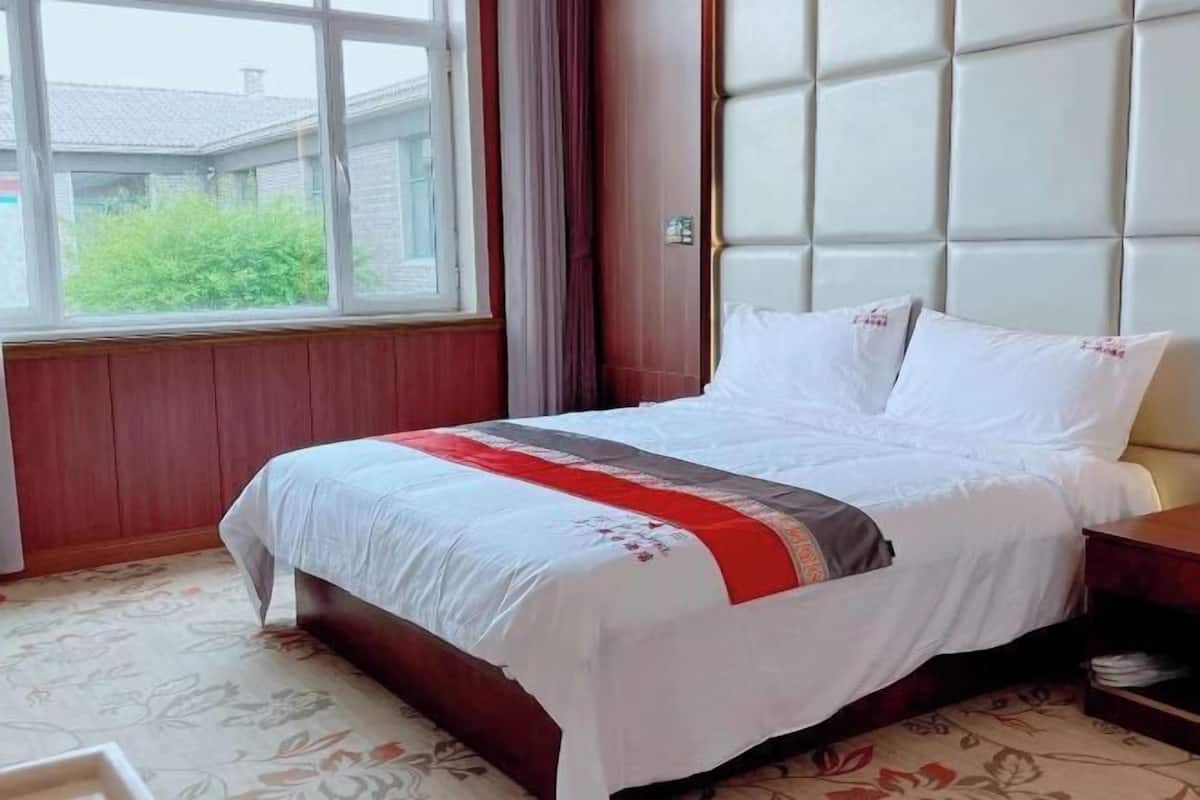 A hotel room with a bed, a window, and a view of greenery outside.