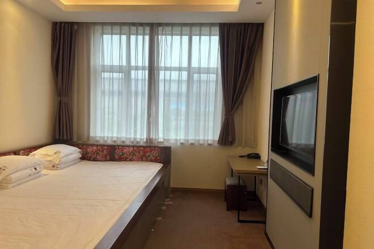 A hotel room with a bed, a desk, a television, and a window with curtains.