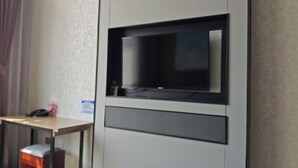 Ein Hotelzimmer mit einem wandmontierten Flachbildfernseher, einem Holztisch und einer kleinen Mülltonne.