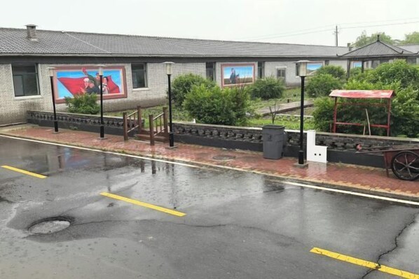 A building with a mural on the side, a covered area with a bench, and a paved area with yellow lines. - Holiday Inn Wulagai Management Area (East Ujimqin Banner)