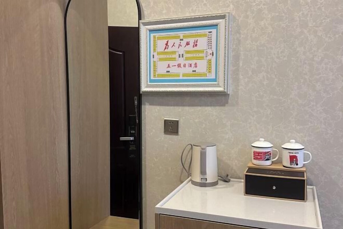 Hotellihuoneessa on seinällä kehystetty kyltti, kahvinkeitin ja tasolla kaksi mukia.