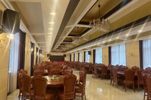 A banquet hall with multiple round tables and chairs, a stage at the front, and a chandelier. - Holiday Inn Wulagai Management Area (East Ujimqin Banner)