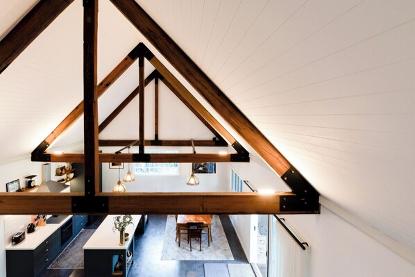 A modern loft with exposed wooden beams, a kitchen area, and a dining space with a view of the city.