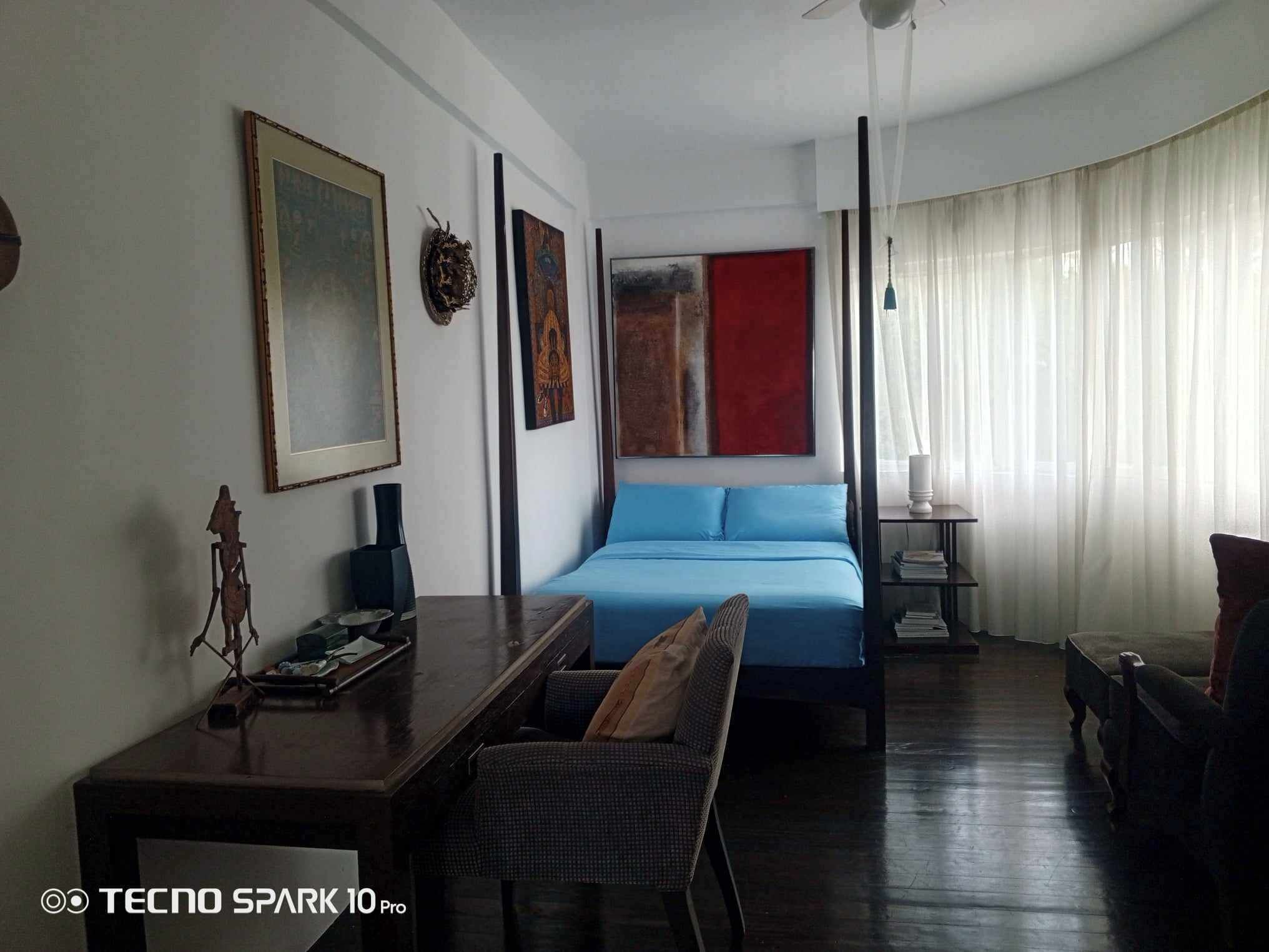 A hotel room with a bed, a desk, a chair, and a bookshelf.