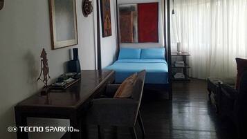 A hotel room with a bed, a desk, a chair, and a bookshelf.