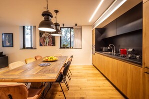 A modern kitchen with wooden cabinets, a dining table with chairs, pendant lighting, and a view of the outdoors.